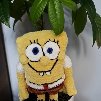 SpongeBob SquarePants plush toy held under a potted plant with green leaves against a white background
