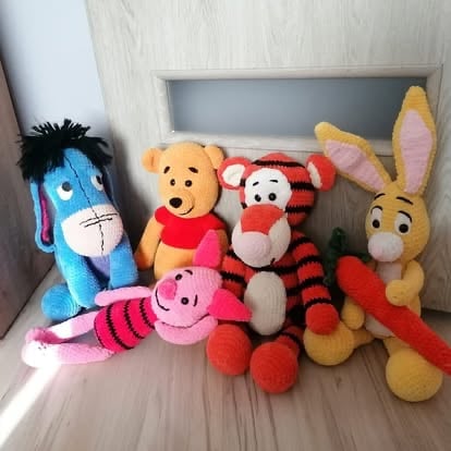 Collection of colorful plush toys including Winnie the Pooh, Eeyore, Tigger, Piglet, and other stuffed animals arranged on a shelf