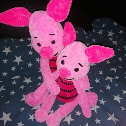 Two pink plush pig toys with embroidered faces sitting together on a dark star-patterned fabric background