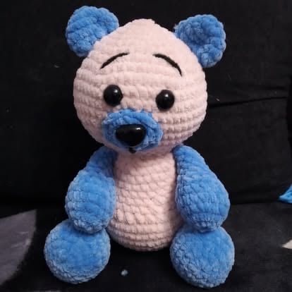 Crocheted blue and white polar bear plush toy with black eyes and nose on dark background