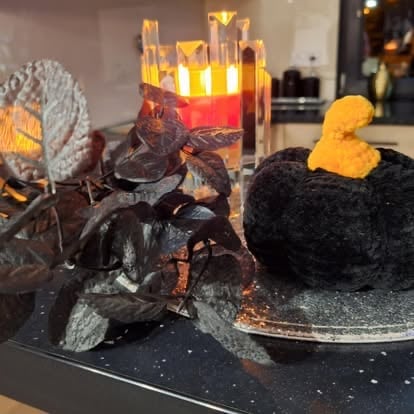 Spooky Halloween decorations on a dark surface including dark flowers, glowing candle holders, and decorative pumpkins
