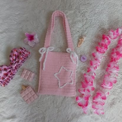 Pink knit tote bag with star design surrounded by matching hair accessories and decorative items on white textile